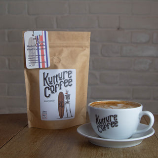 Kulture Coffee package and cup on a wooden table with a brick wall background